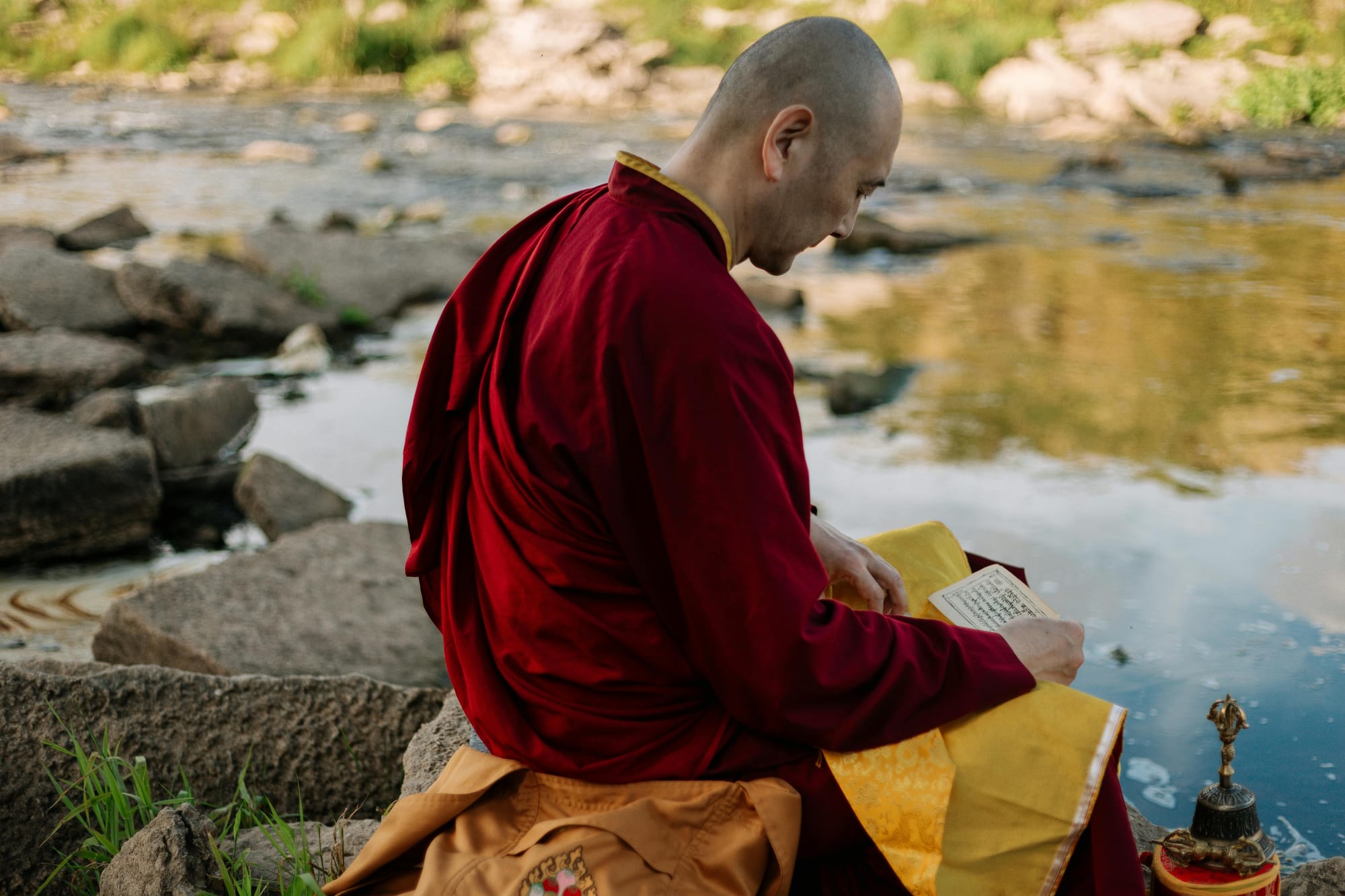 A monk reading a book by the river