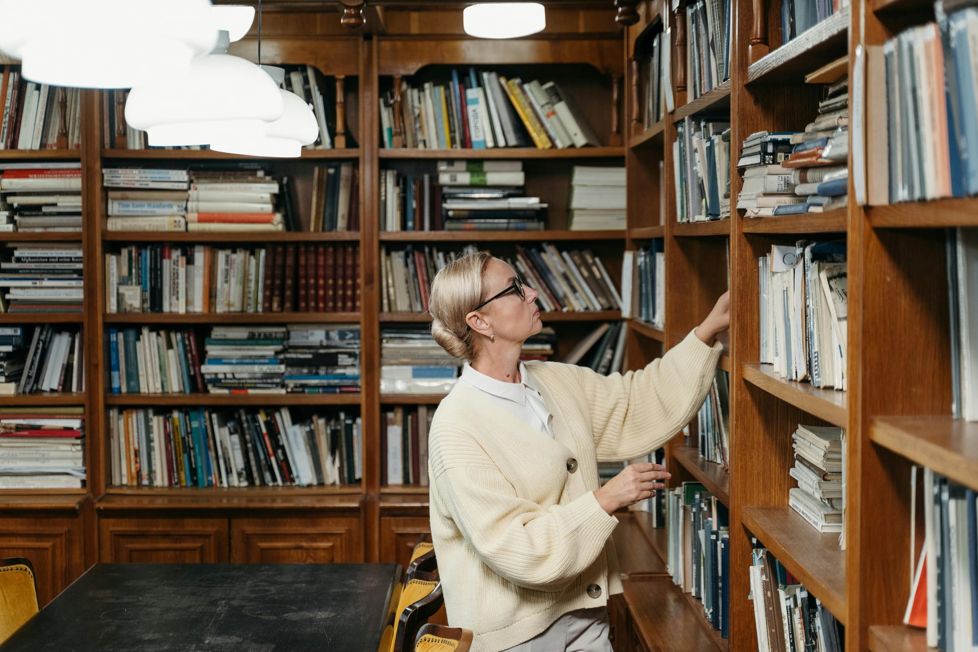 a woman with glasses chooses a book in an old library