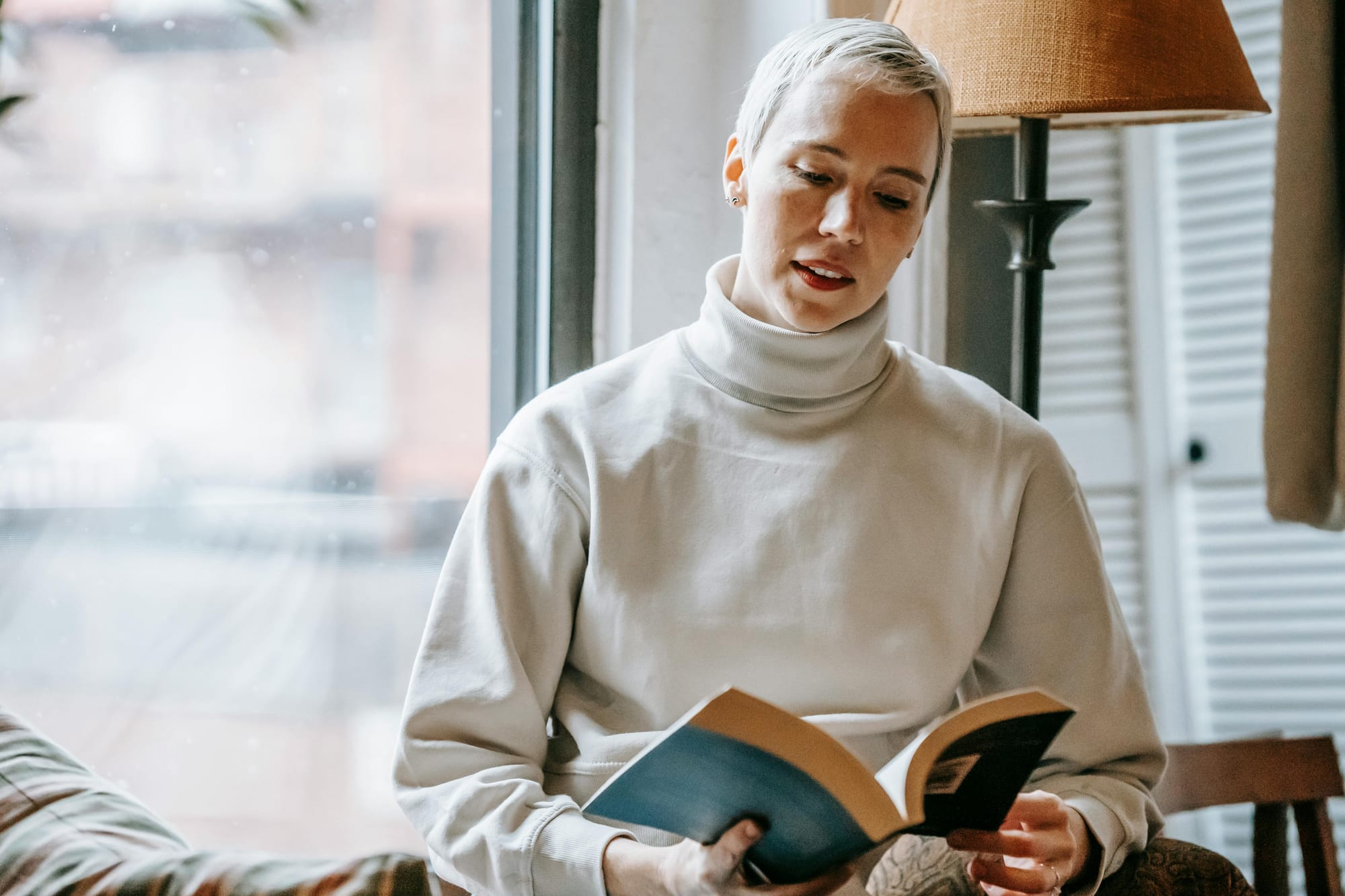 slightly smiling woman reading an interesting book near the window