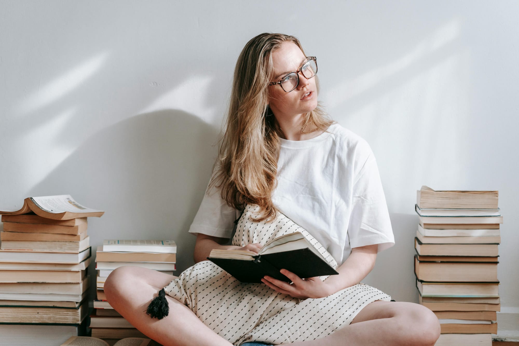 woman reading a book on the floor surrounded by piles of books