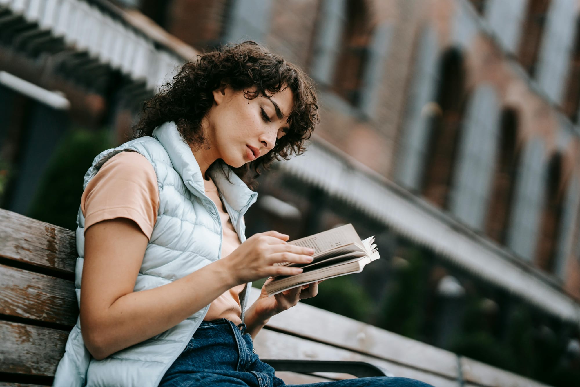 thoughtful young woman reading a book on a bench