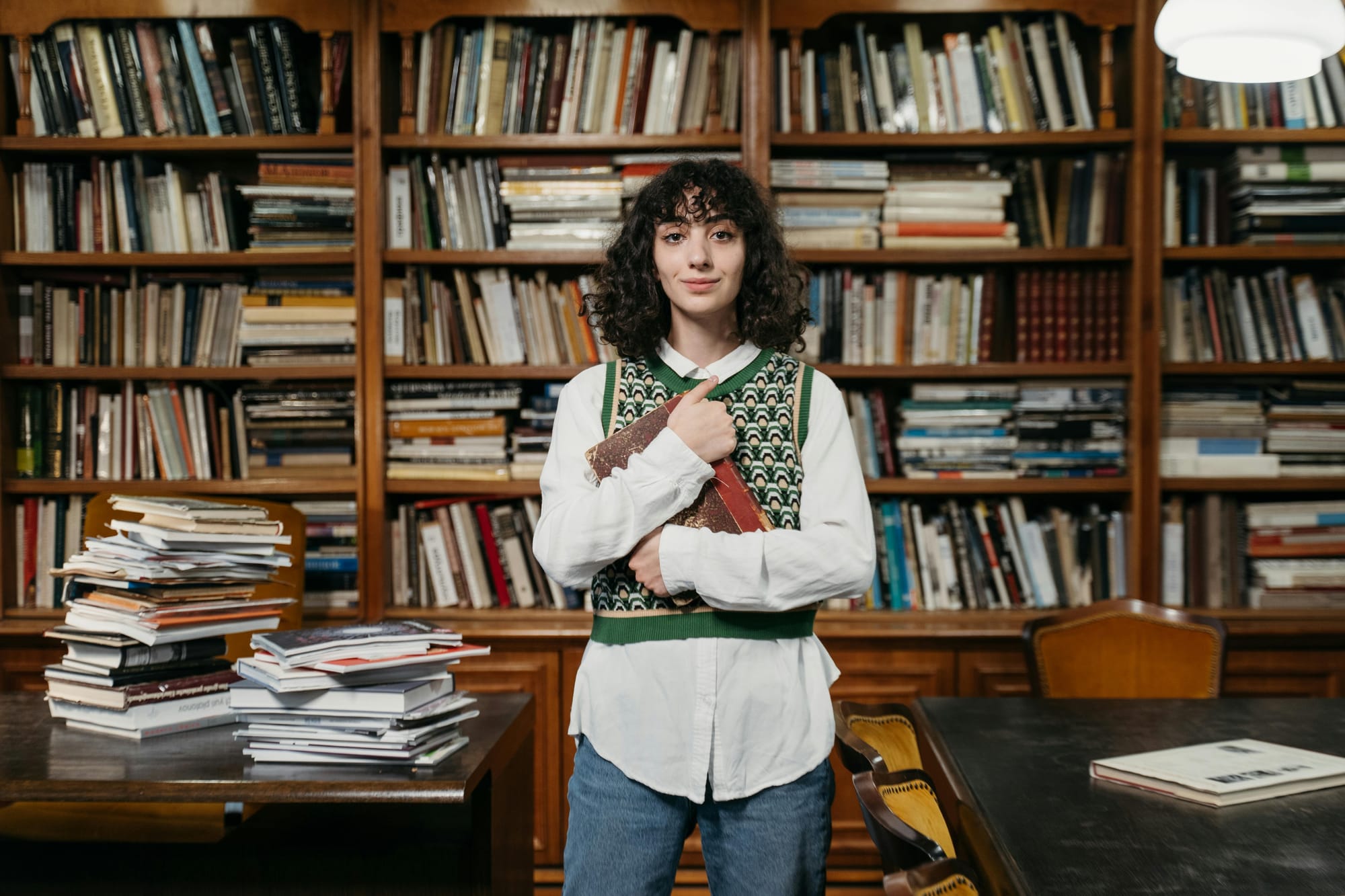 woman holding an old book close to her chest in a library full of books