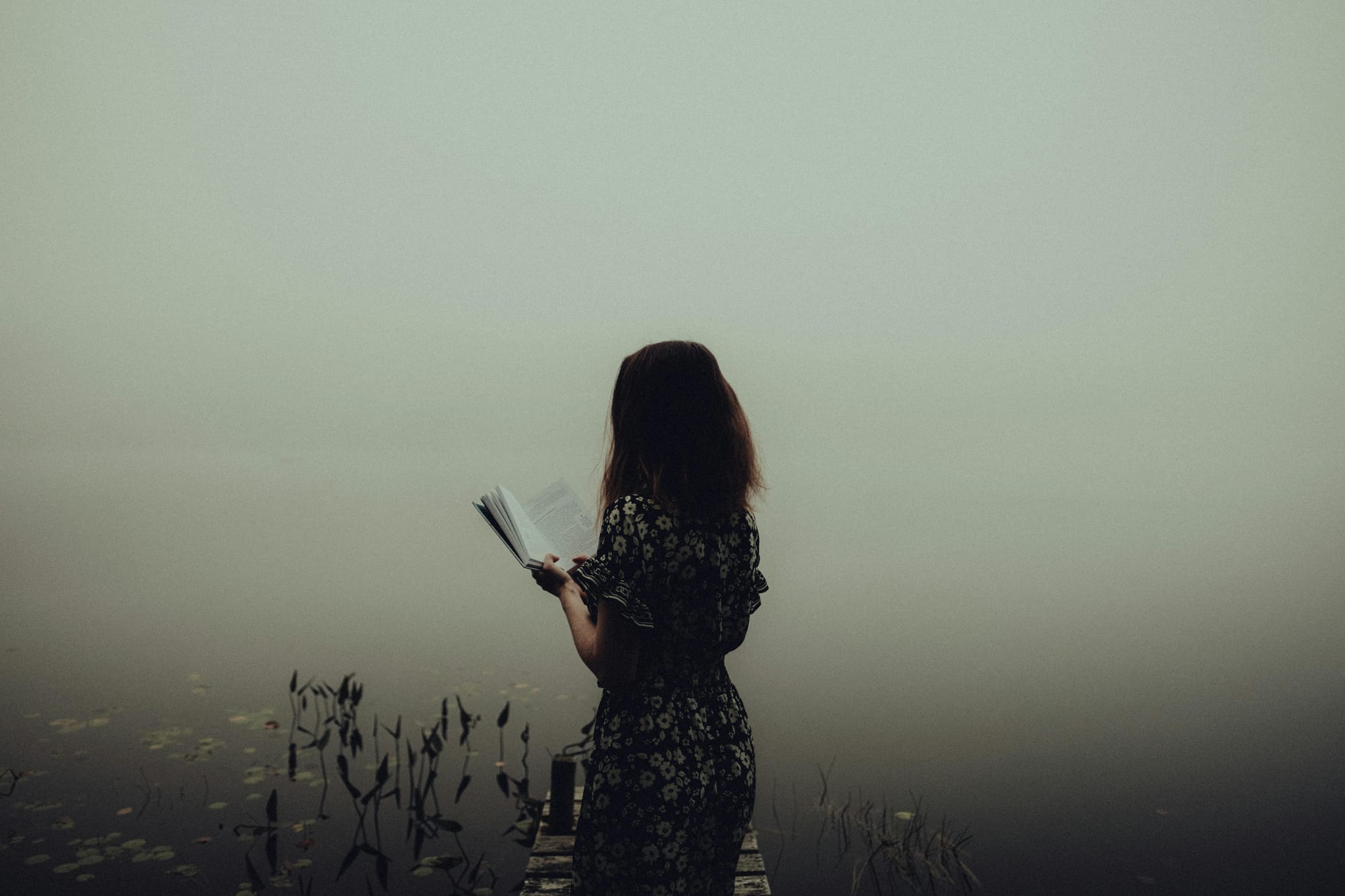 woman reading a book near a lake in the fog