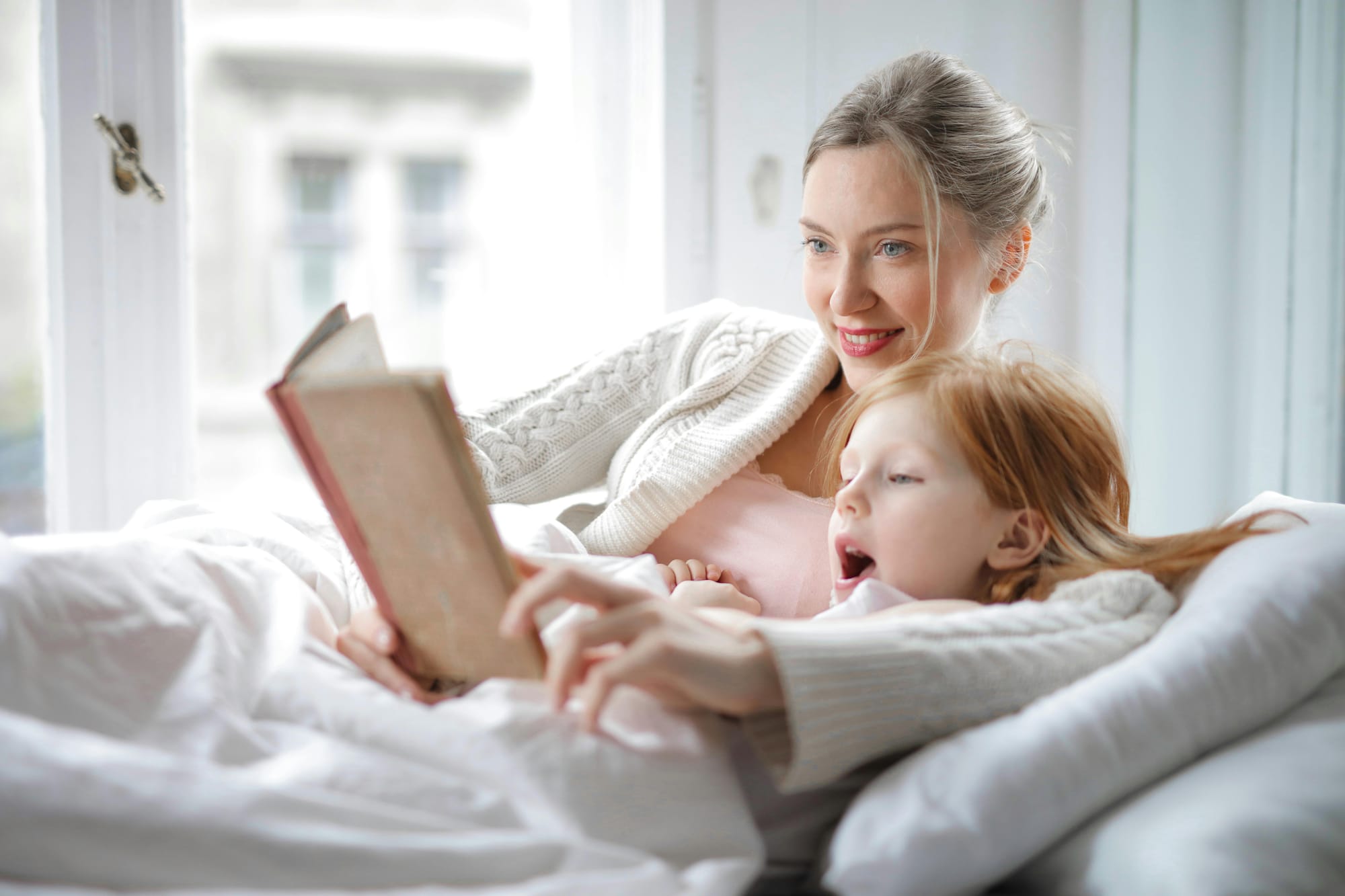 mother and daughter lying in bed reading a book