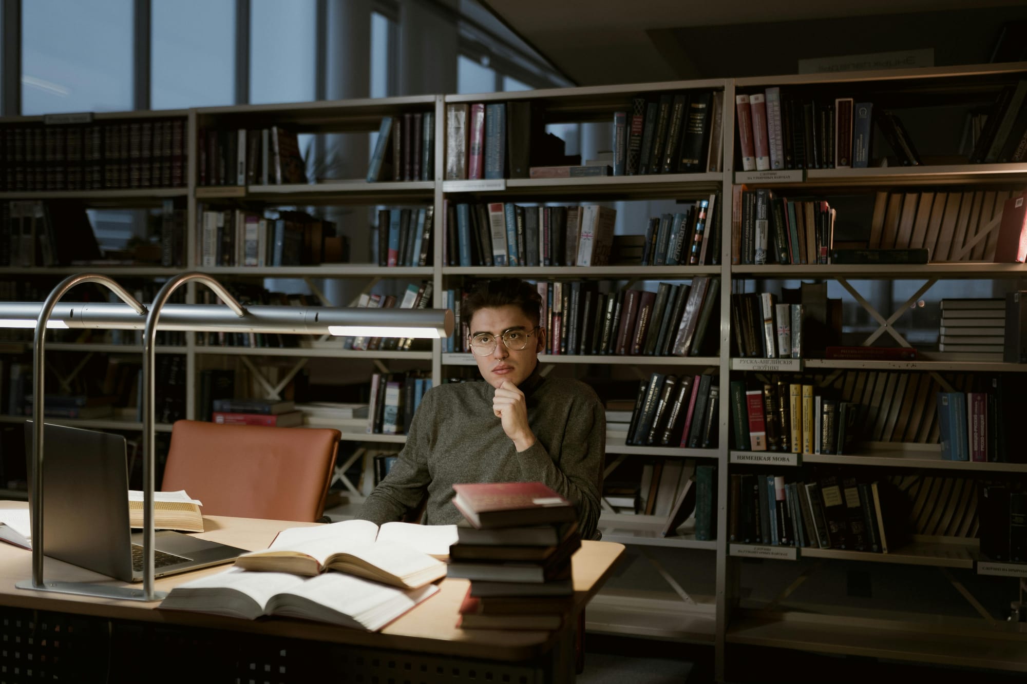 a thoughtful man with glasses sitting in a library