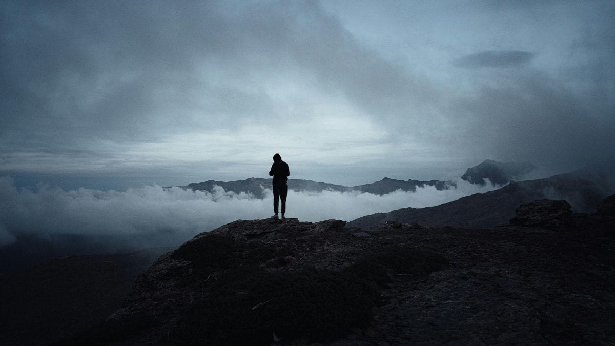 Person standing on mountain top above the clouds at sunrise or sunset.