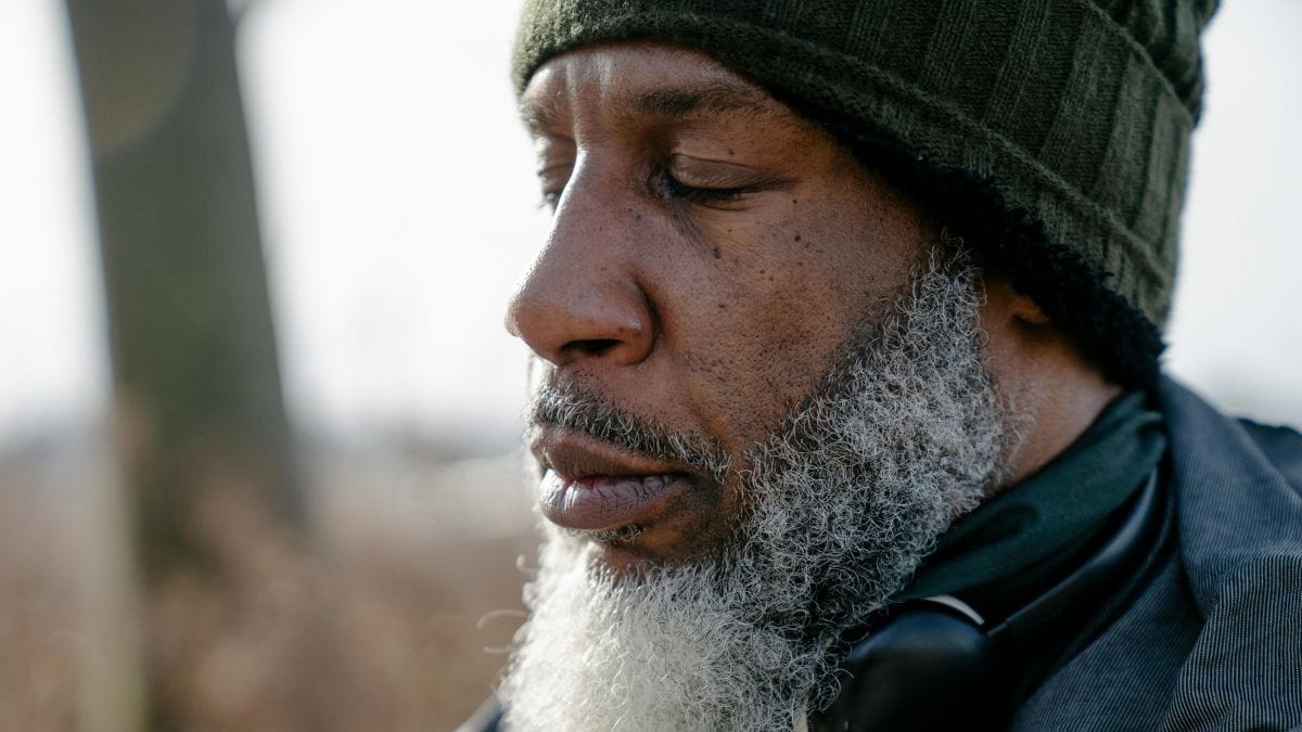 Elderly man with a beard standing outside with his eyes closed